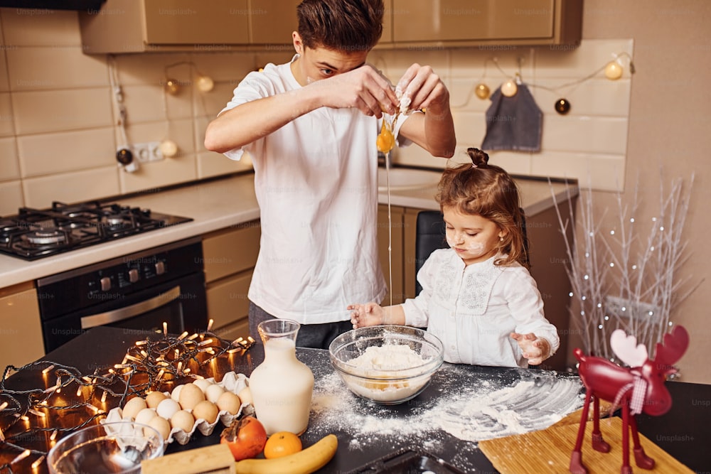 Hermano con su hermana pequeña preparando comida en la cocina y divirtiéndose.