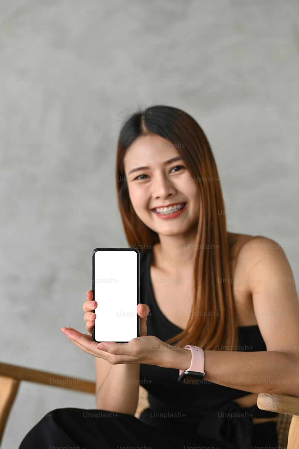 空の画面でスマートフォンを示す若いアジアの女性の肖像画。
