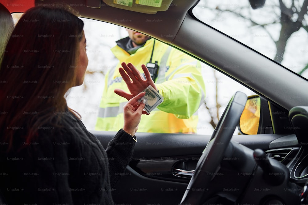 Un policier en uniforme vert refuse d’accepter un pot-de-vin d’une femme dans un véhicule.