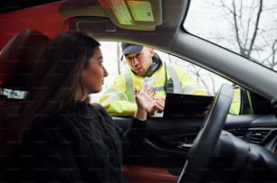 Male police officer in green uniform checking vehicle on the road. Woman trying to give bribe.