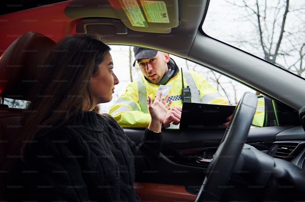 Policial do sexo masculino em uniforme verde verificando veículo na estrada. Mulher tentando dar suborno.