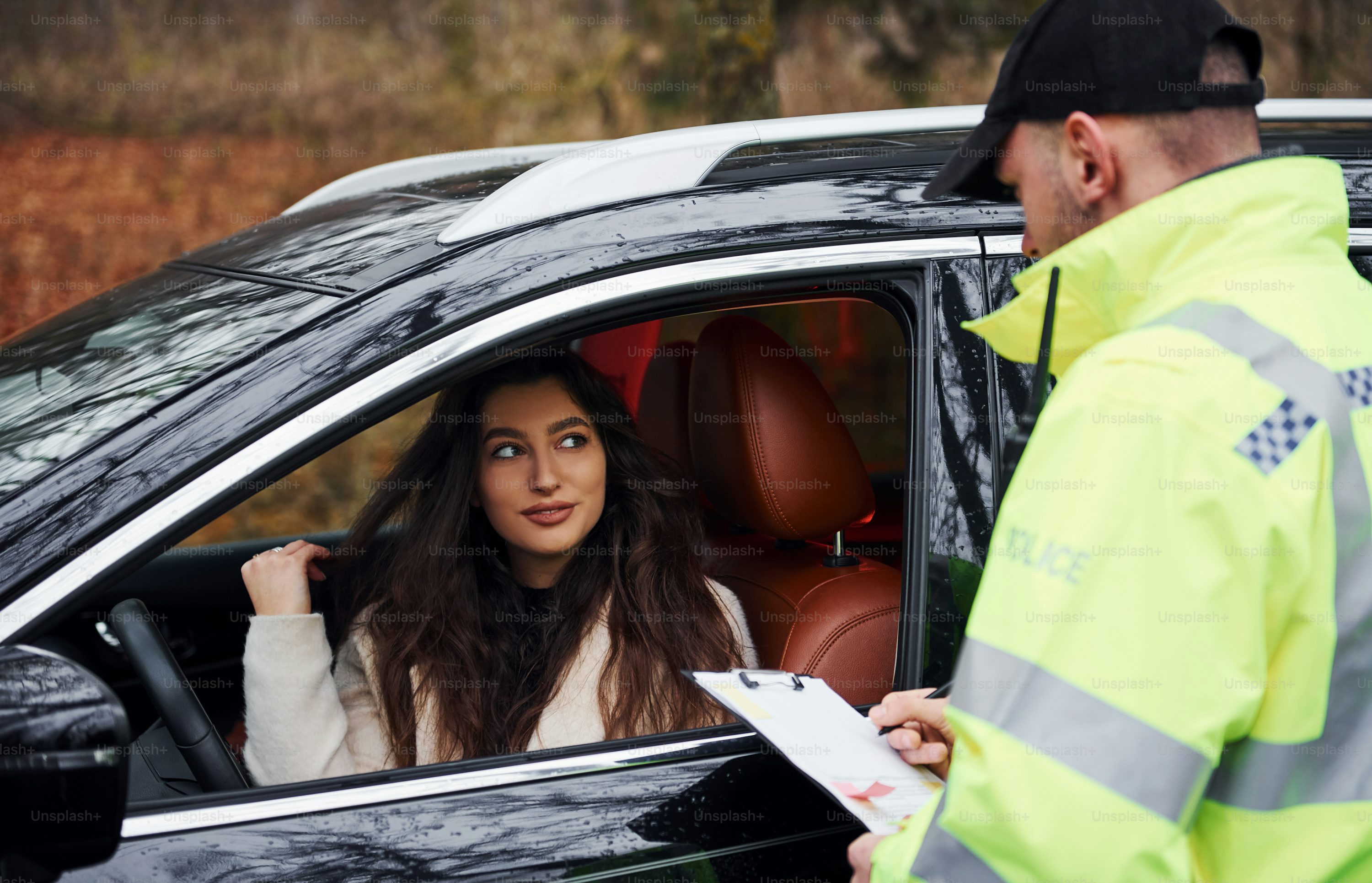 Male police officer in green uniform with notepad checking vehicle on the road.