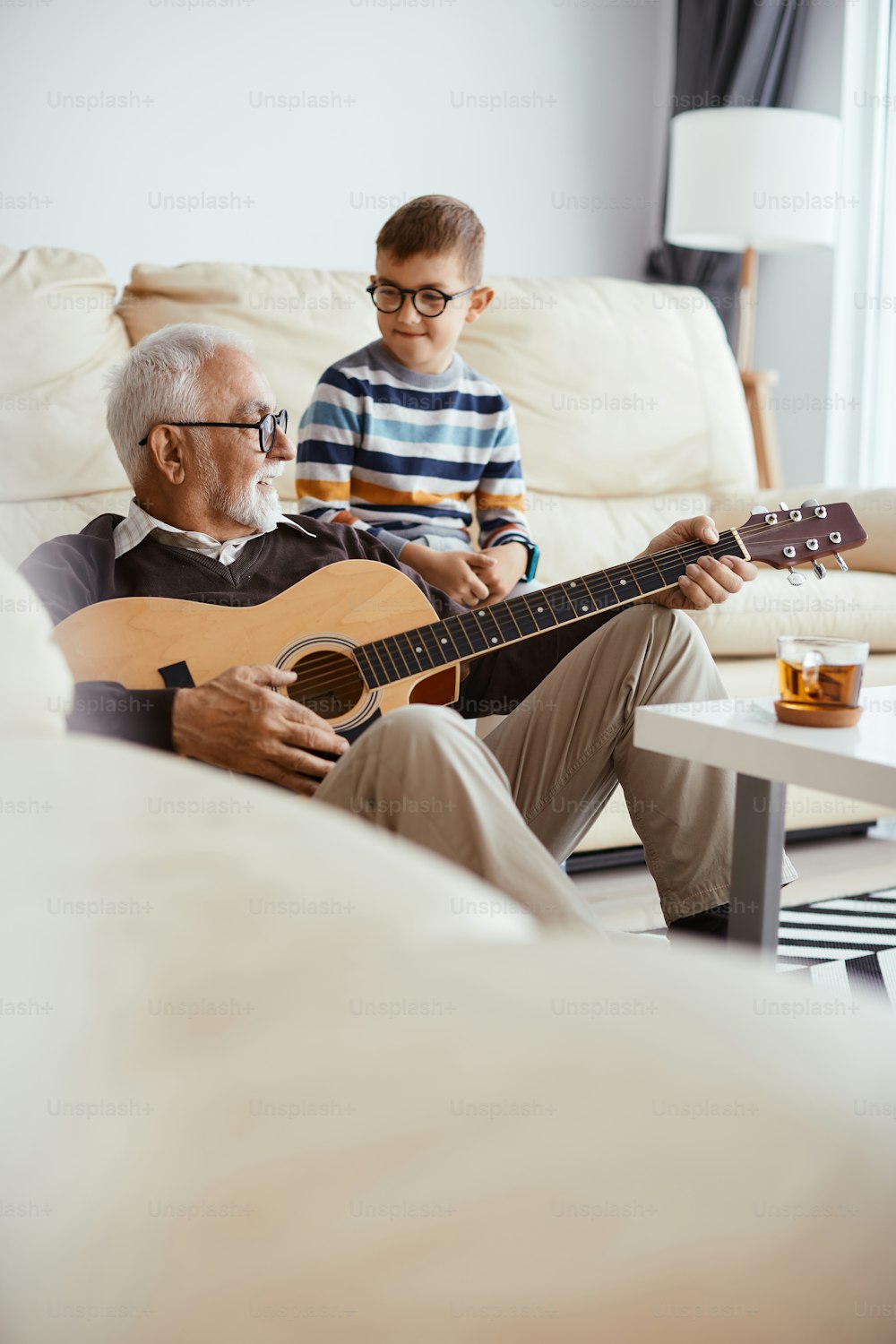 Happy grandfather playing acoustic guitar while spending time with his grandson at home.