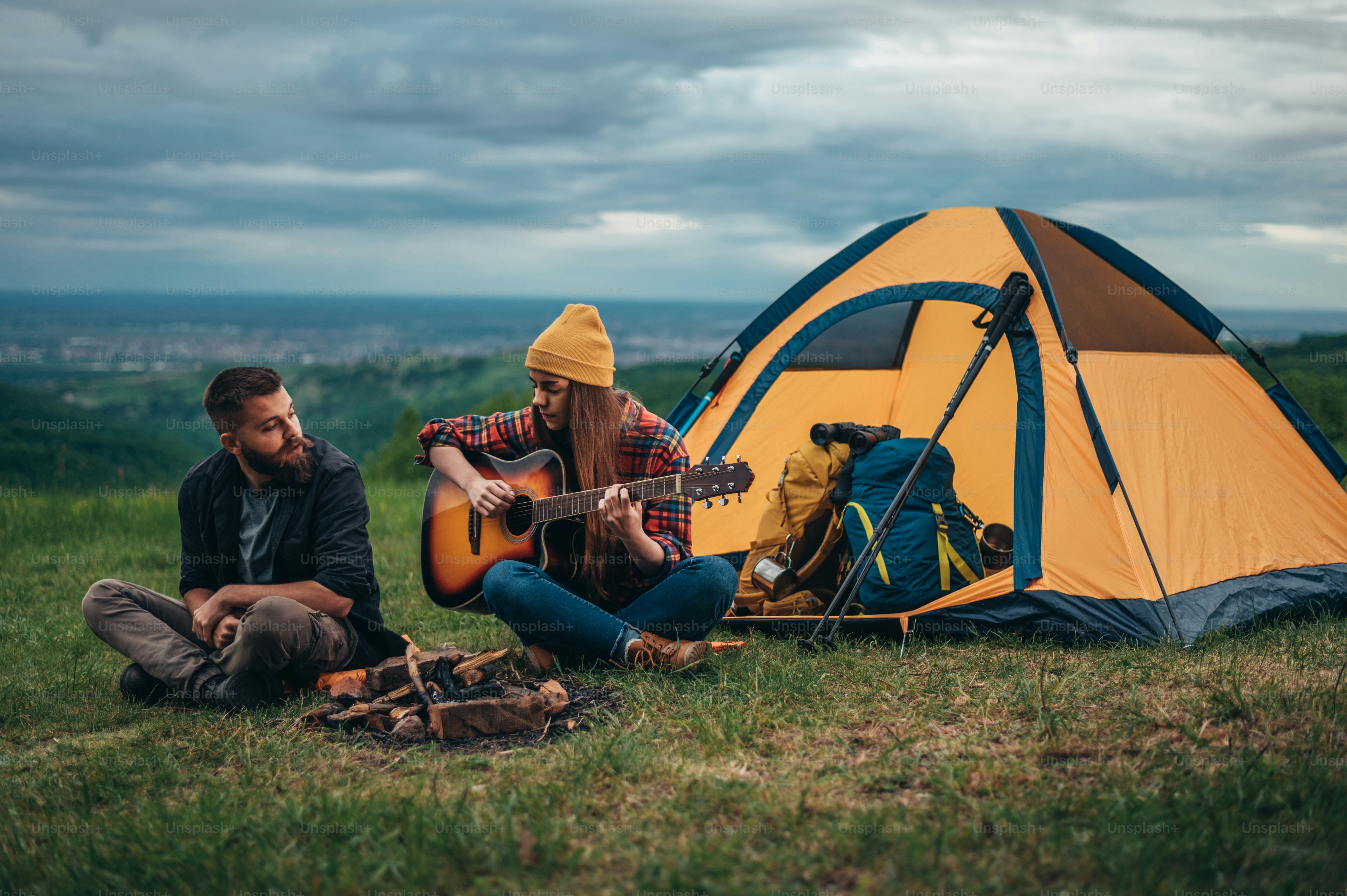 Young couple of campers sitting near the tent in a camp and playing a guitar while having fun