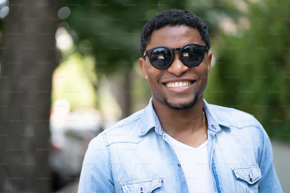 Homem afro-americano usando óculos escuros e sorrindo enquanto estava ao ar livre na rua.