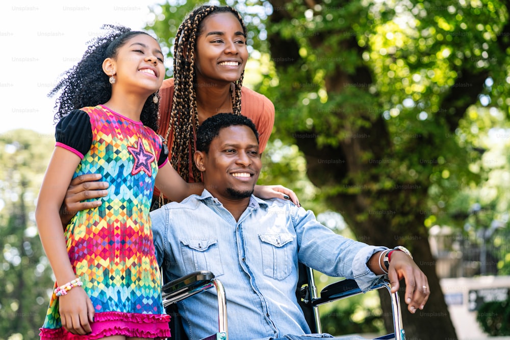 An african american man in a wheelchair enjoying a walk outdoors on the street with his family.