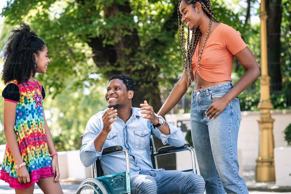 An african american man in a wheelchair having a good time while enjoying with his family outdoors on the street.