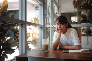 モダンなコーヒーショップに座ってカメラに微笑む若いアジア人女性。