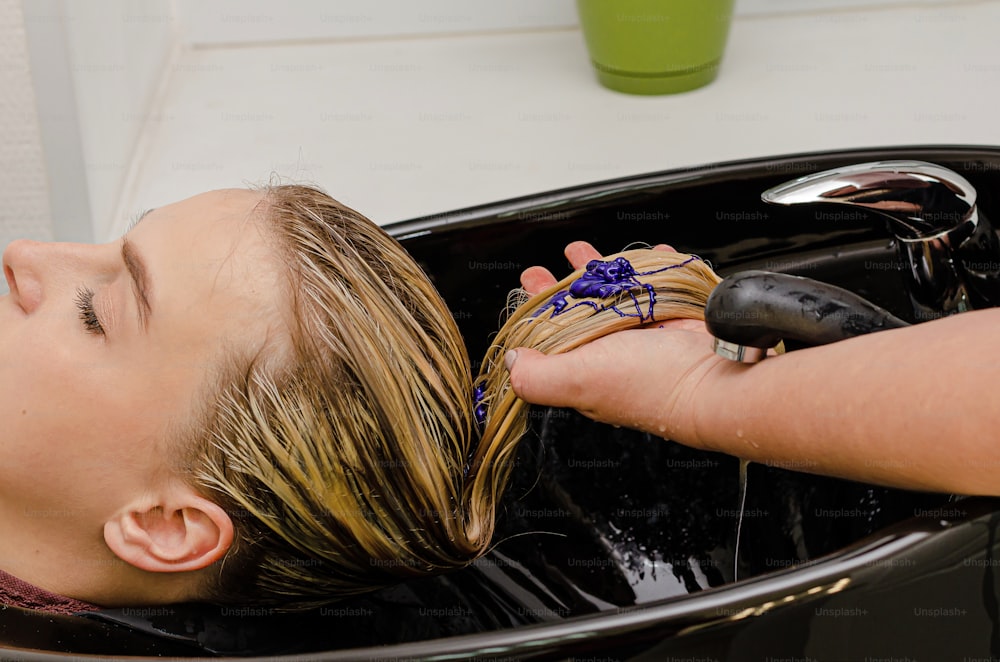 Hair stylist applying coloring purple shampoo after hair dyeing.