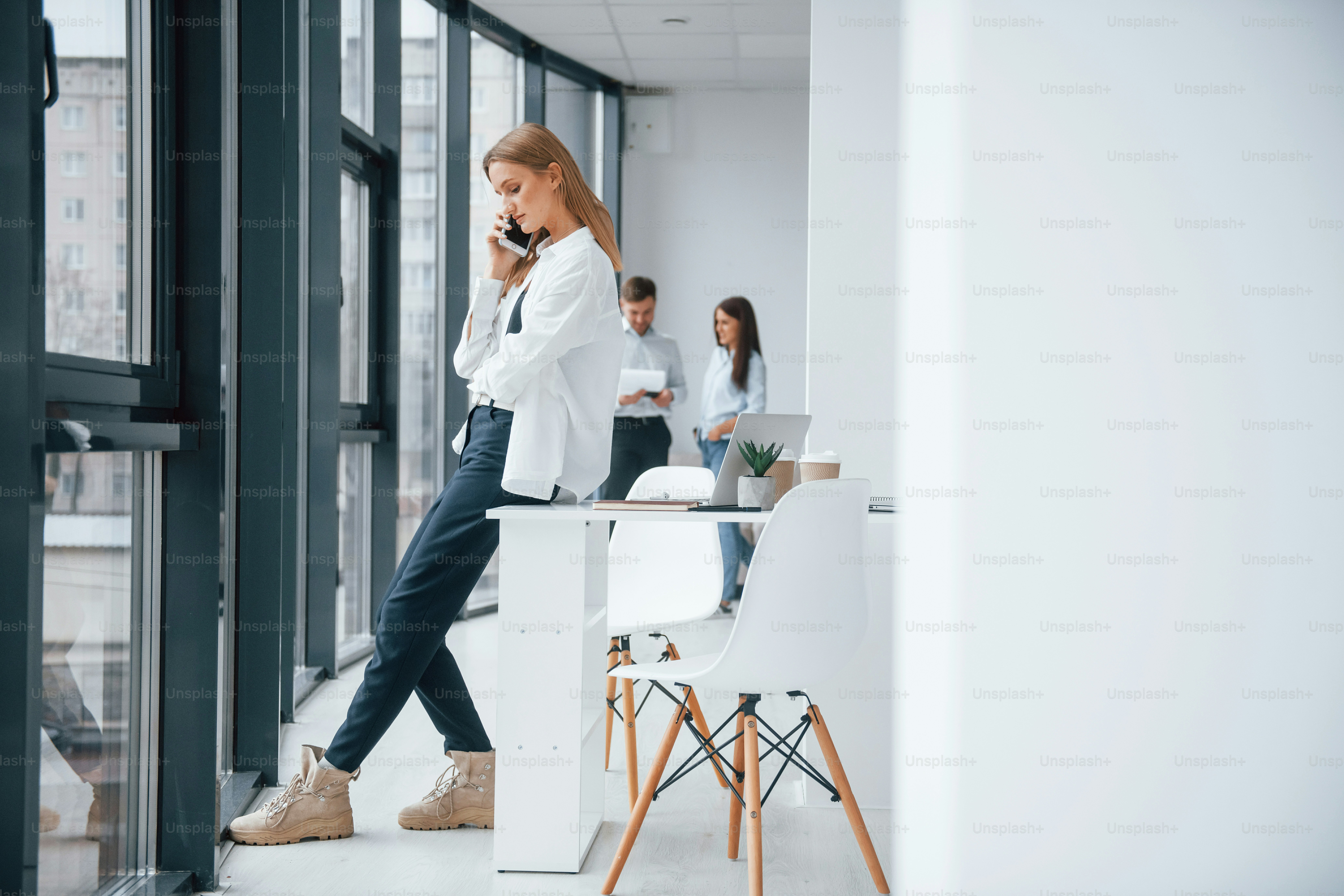 Woman talking by phone in front of group of young successful team that working and communicating together indoors in office.