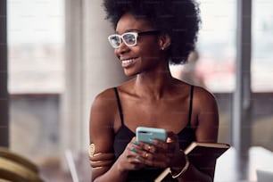 Cheerful african american woman holding smartphone and notepad.