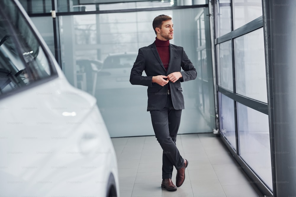 Young business man in luxury suit and formal clothes is indoors near the car.