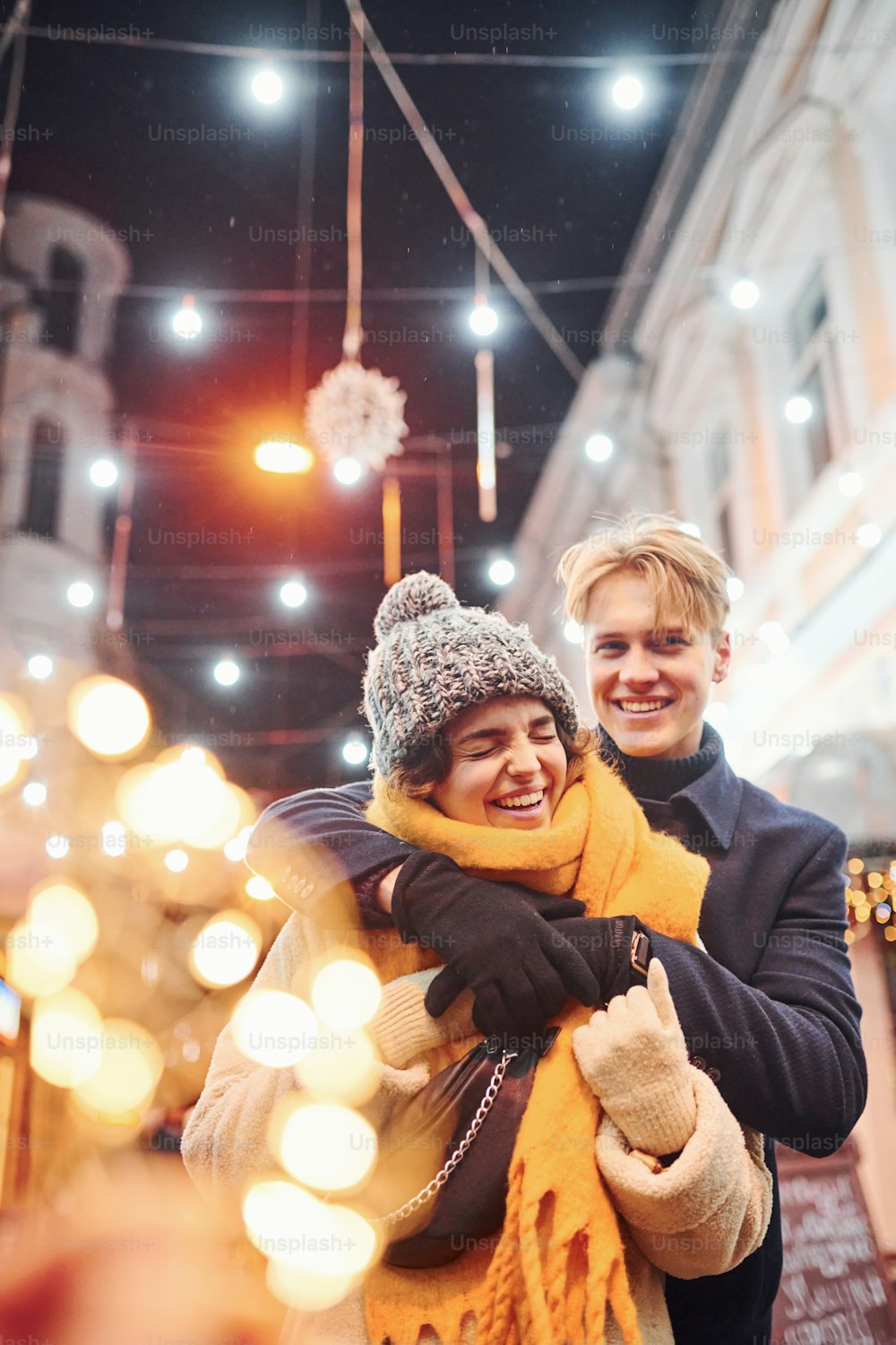 La giovane coppia felice in vestiti caldi è sulla strada decorata di Natale insieme.