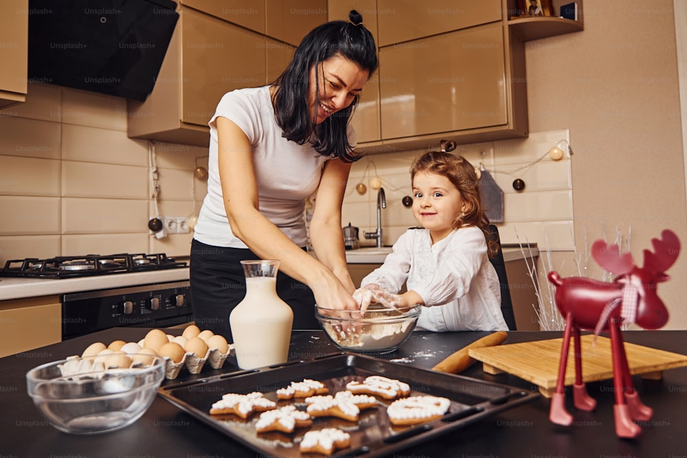 Mother with her little daughter preparing food on kitchen and have fun.