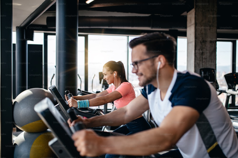 Young and attractive woman and man biking in the fitness gym. They exercising legs and doing cardio workout while riding cycling machines.