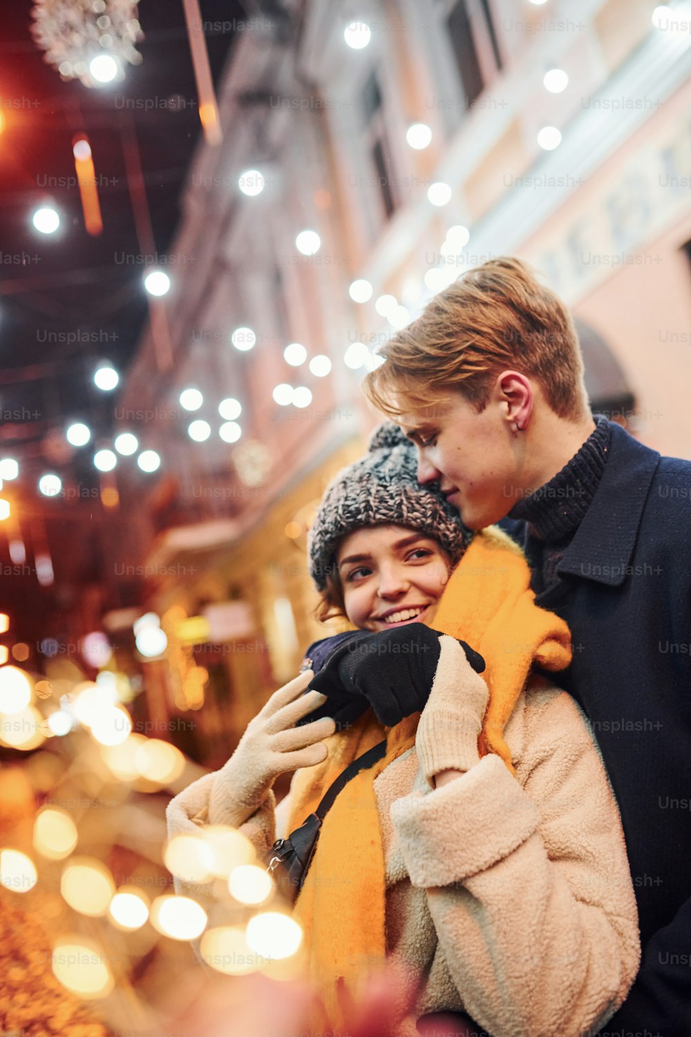 Happy young couple in warm clothes is on christmas decorated street together.
