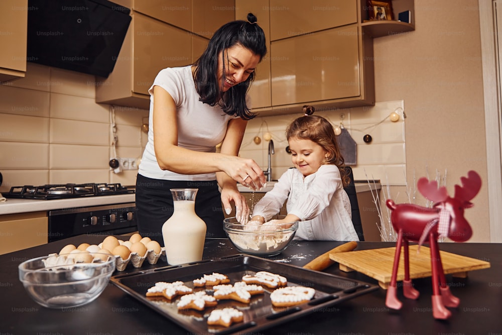 Mãe com sua filhinha preparando comida na cozinha e se divertindo.