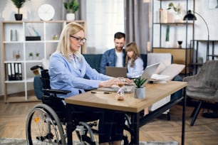 Side view of attractive woman with special needs sitting at table and working on wireless laptop. Husband with daughter playing on computer. Concept of disability, freelance and family support.