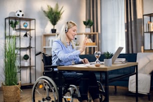 Charming woman with special needs talking and gesturing during video conference on modern laptop. Young blonde working remotely while staying at home.