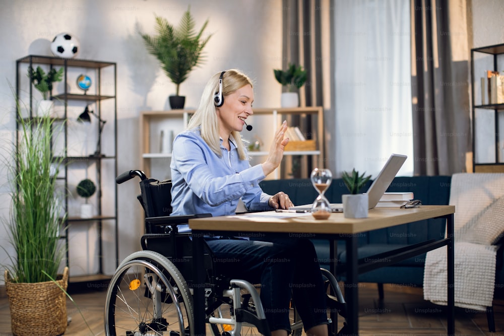 Charming woman with special needs talking and gesturing during video conference on modern laptop. Young blonde working remotely while staying at home.