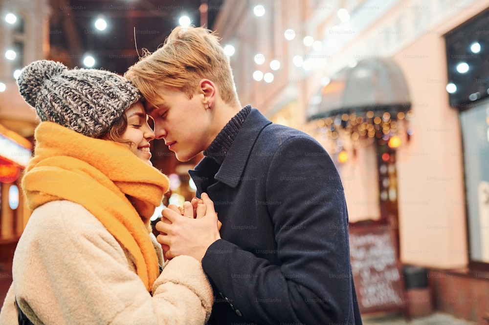 Closeness of the people. Happy young couple in warm clothes is on christmas decorated street together.