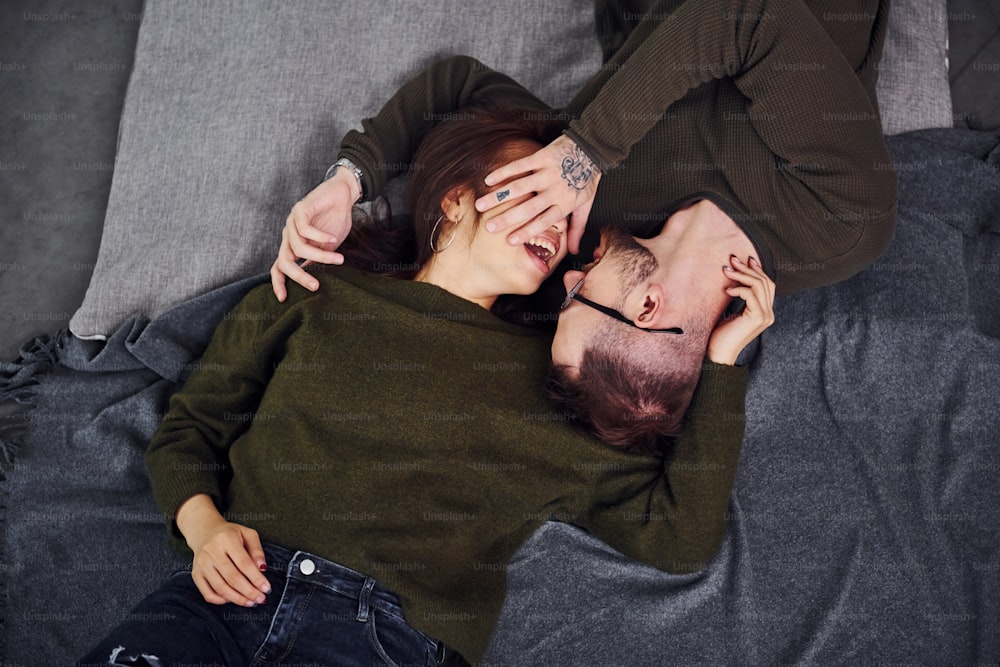 Happy multi ethnic couple in casual clothes lying down together indoors in the studio. Caucasian guy with asian girlfriend.
