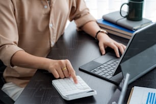 Image of businesswoman sitting in the office using a calculator and a tablet with accounting document.