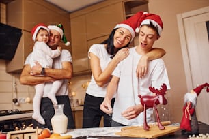 La familia festiva en sombreros navideños se divierte en la cocina y prepara la comida.
