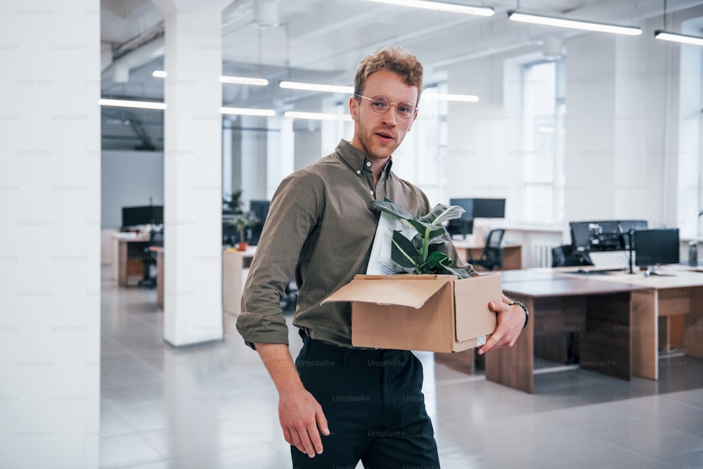 Office worker in formal wear walking with box with green plant inside of it.
