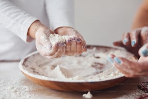 Close up view of woman with her granddaughter preparing food with flour on kitchen.