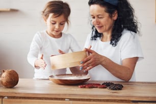 Senior woman with her granddaughter preparing food with flour on kitchen.
