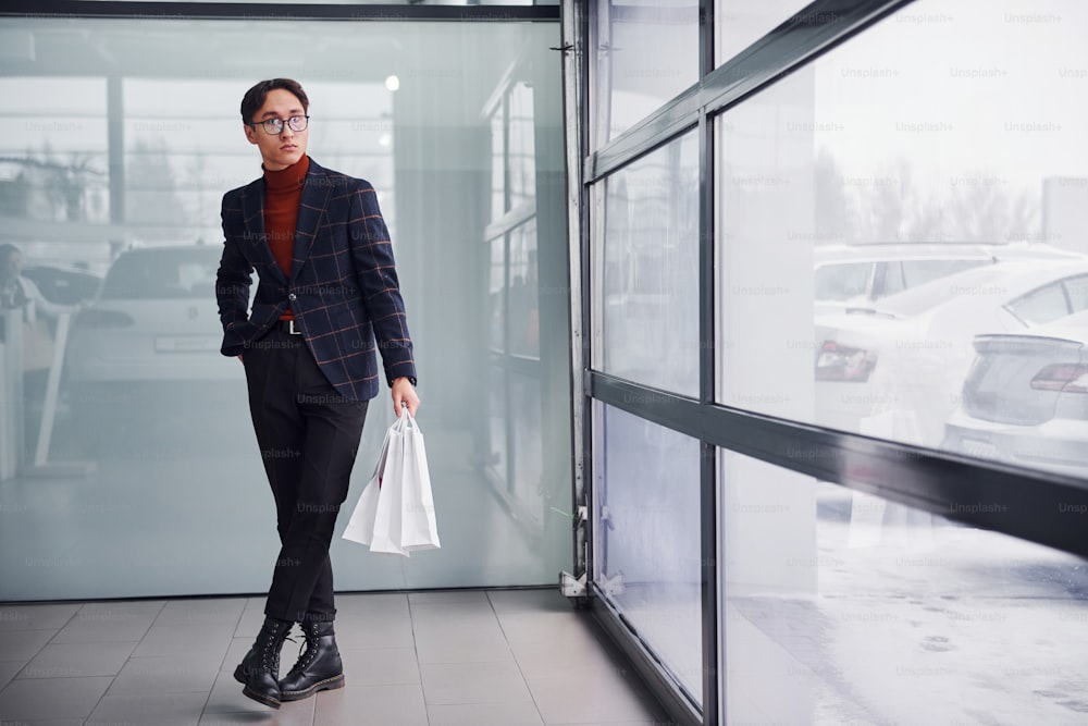 With shopping bags. Young business man in luxury suit and formal clothes is indoors in the office.