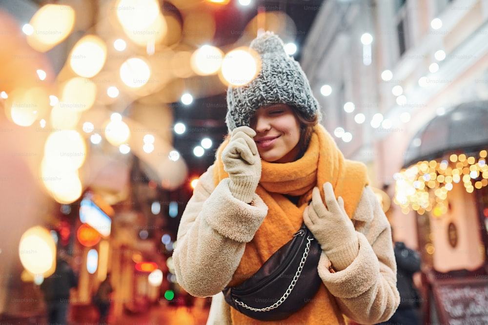 Cheerful young girl in warm clothes have a walk on the christmas decorated street in the city.