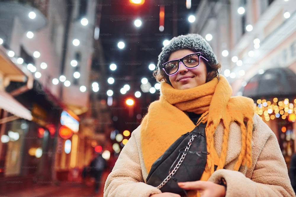 Cheerful young girl in eyewear and warm clothes have a walk on the christmas decorated street in the city.