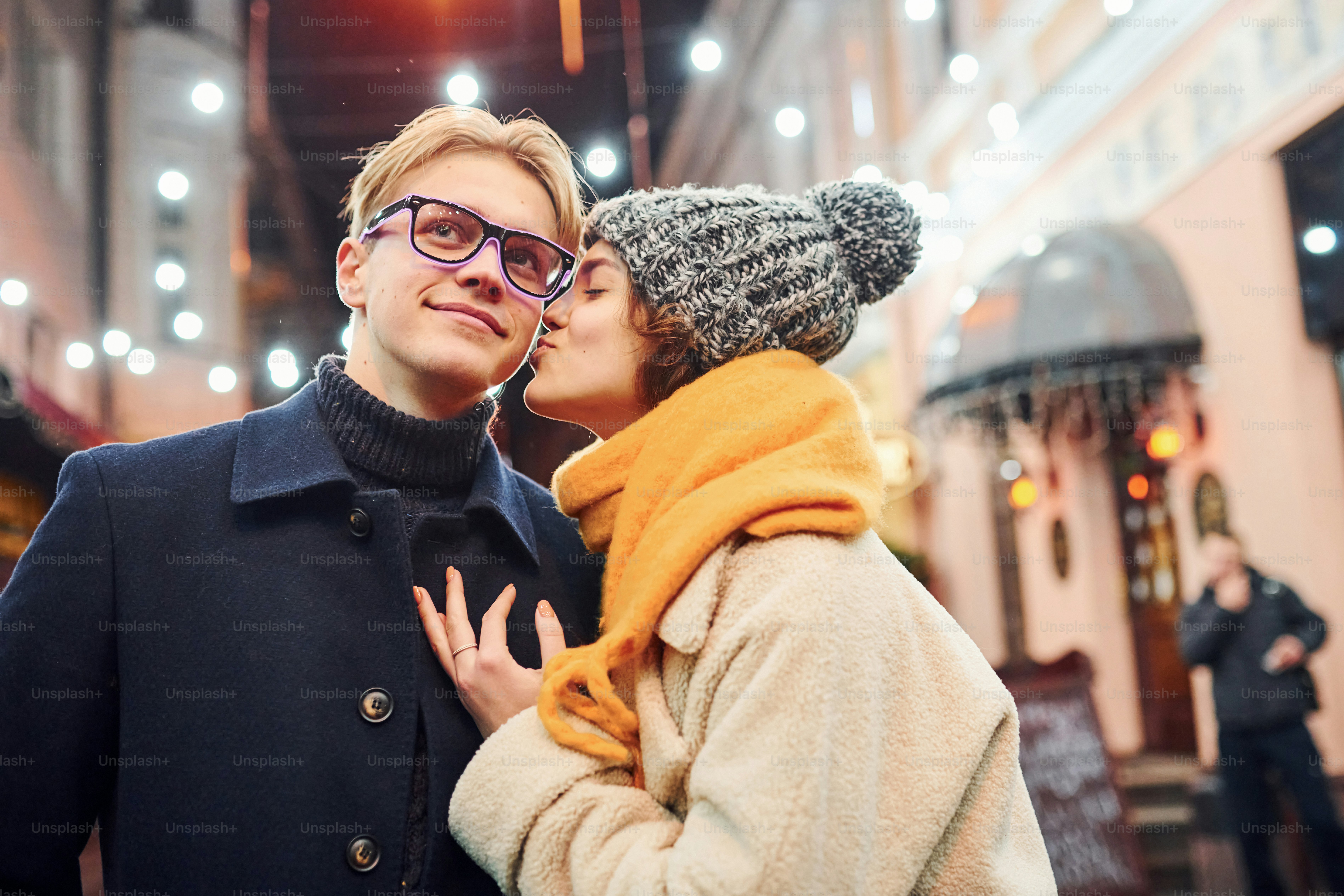 Young girl standing on christmas decorated street and kisses her boyfriend.