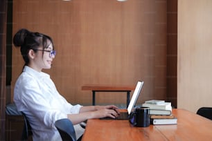 Side view of smiling woman designer sitting in office and working with laptop computer.