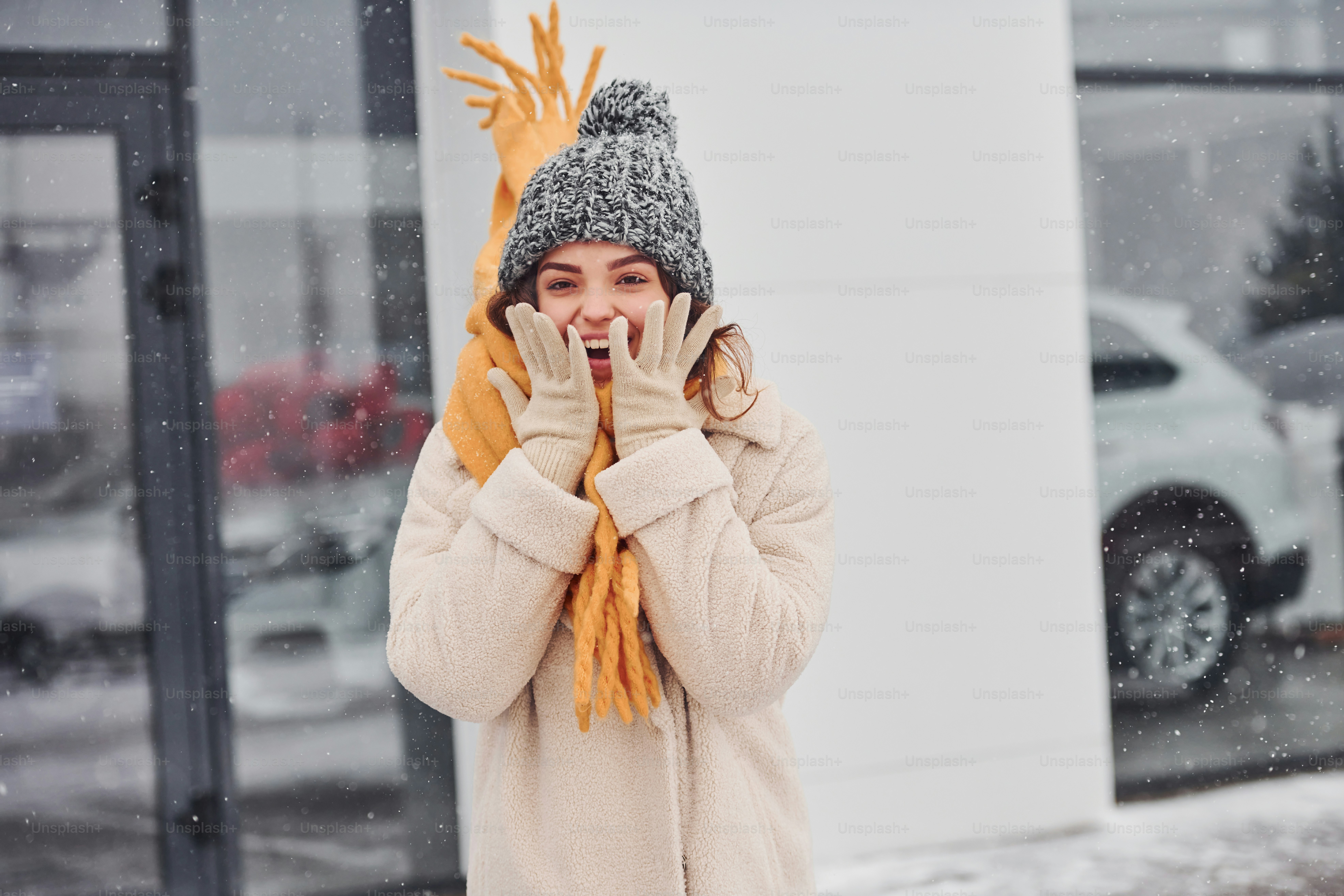 Cheerful young girl smiling standing and smiling outdoors. Snow is falling.