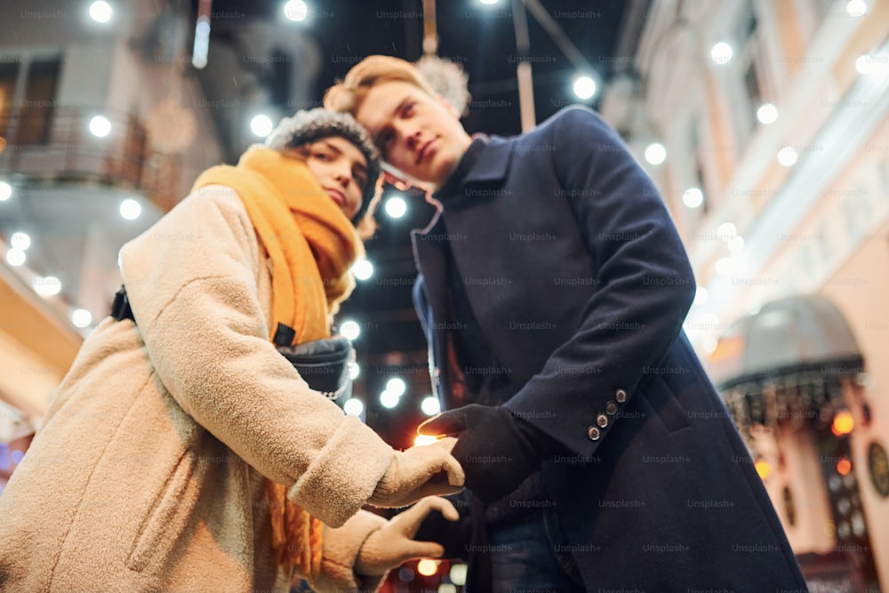 Cercanía de la gente. Una pareja joven feliz con ropa de abrigo está en la calle decorada de Navidad juntos.