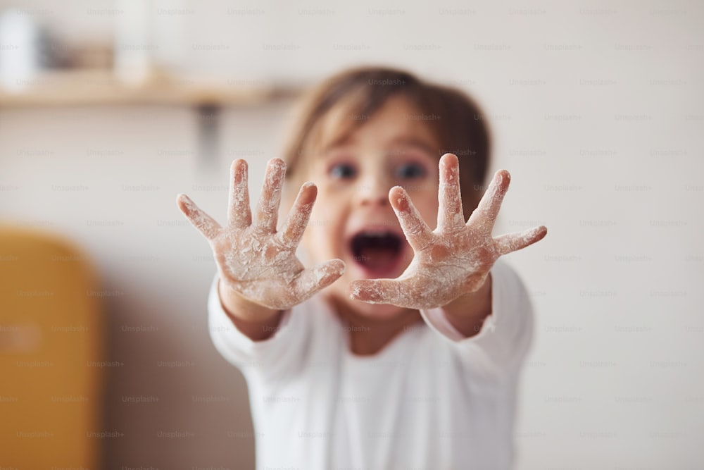 Positive little girl showing hands with flour on in on the kitchen.