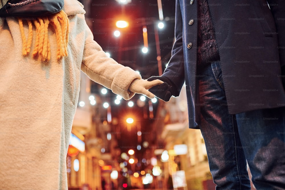 Close up view of young couple in warm clothes that is on christmas decorated street together.