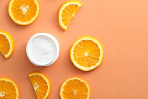 色の背景に柑橘系のフルーツクリーム保湿剤とオレンジスライス。フラットレイ、上面図。