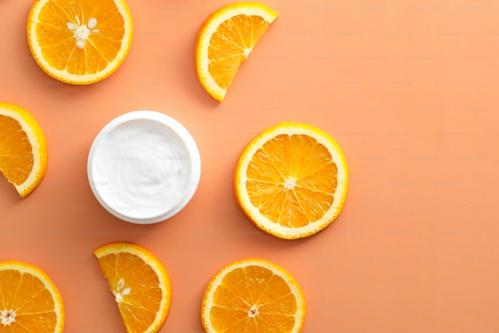 Citrus fruit cream moisturizer and orange slices on color background. Flat lay, top view.