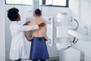Junge afrikanische Ärztin Radiologin oder Röntgentechnikerin, die Thoraxröntgenscans eines jungen männlichen Patienten in einem modernen Untersuchungsraum durchführt
