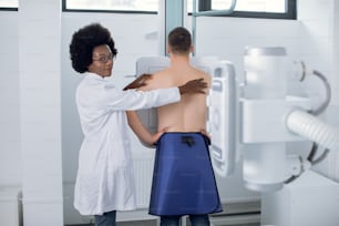 Junge afrikanische Ärztin Radiologin oder Röntgentechnikerin, die Thoraxröntgenscans eines jungen männlichen Patienten in einem modernen Untersuchungsraum durchführt