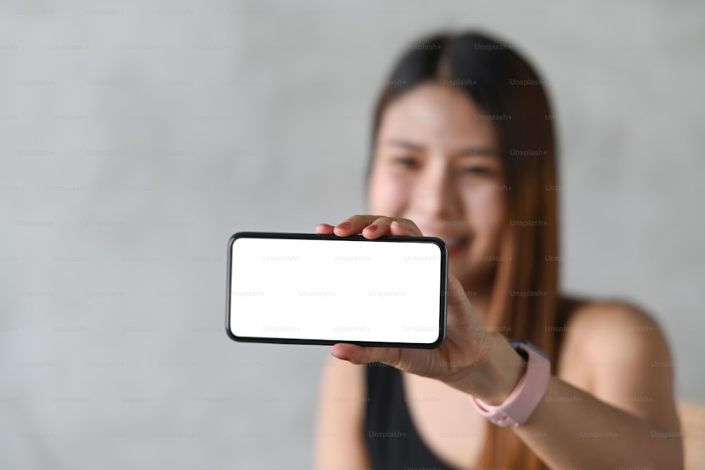 Femme heureuse montrant un téléphone portable horizontal avec un écran vide.