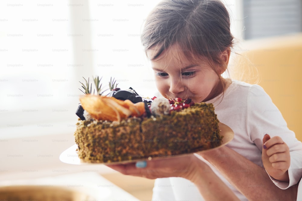 Cheerful little girl eating fresh dietical cake on the kitchen.