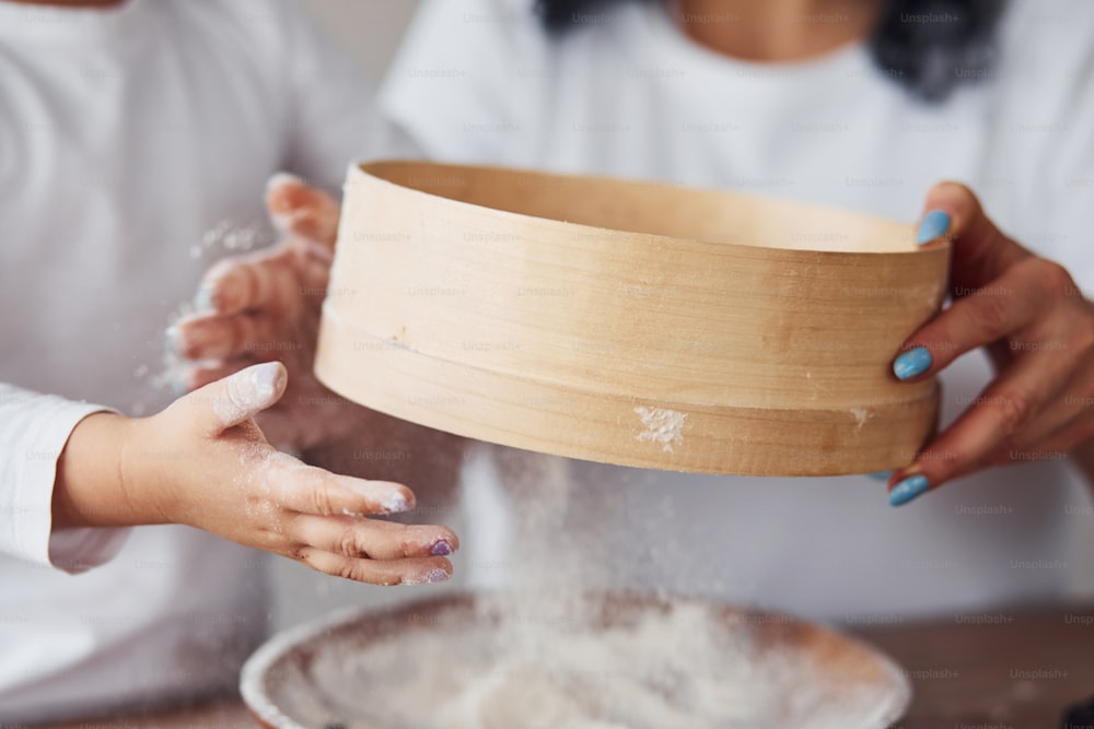 Close up view of woman with her granddaughter preparing food with flour on kitchen.