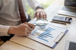 Businessman looking at growth chart with magnifying glass.