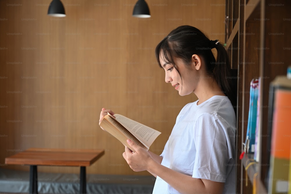 Side view of young asian woman reading book in library.