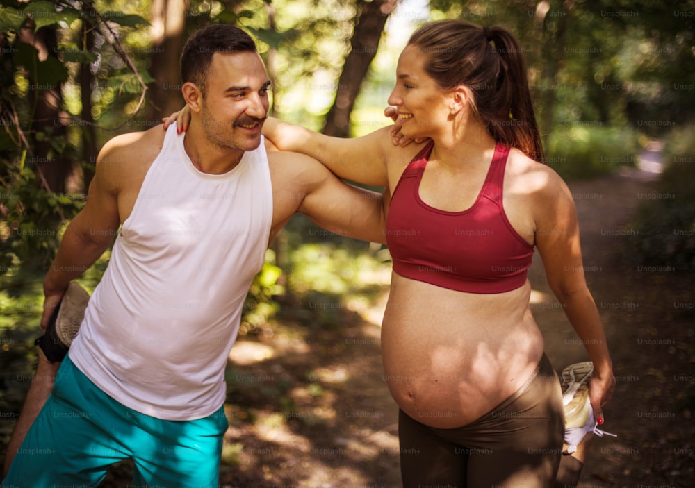 The coach helps a pregnant woman during exercises in the park.